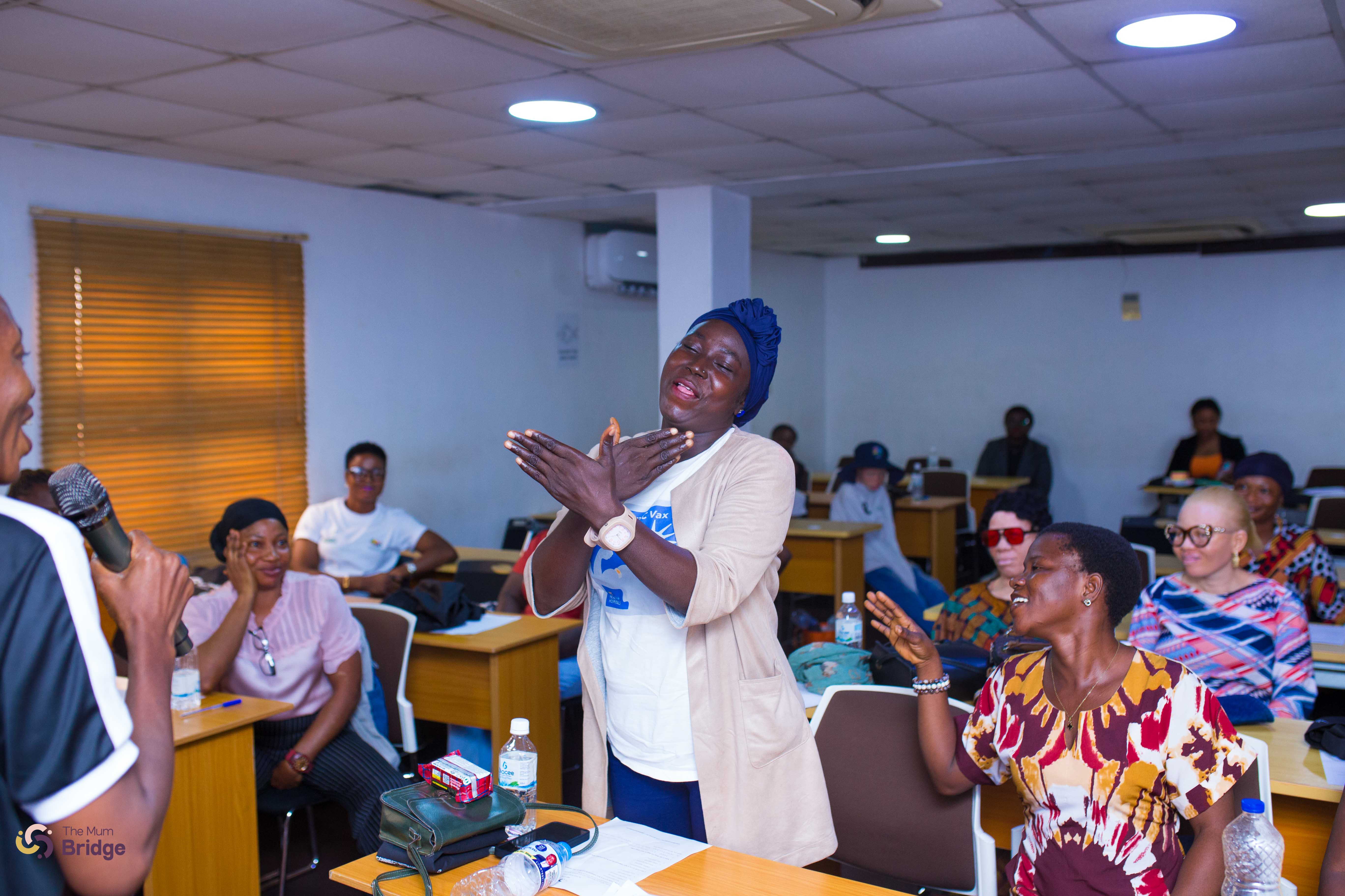 A mother celebrates joyfully with clasped hands as her community cheers around her during a Mum Bridge session