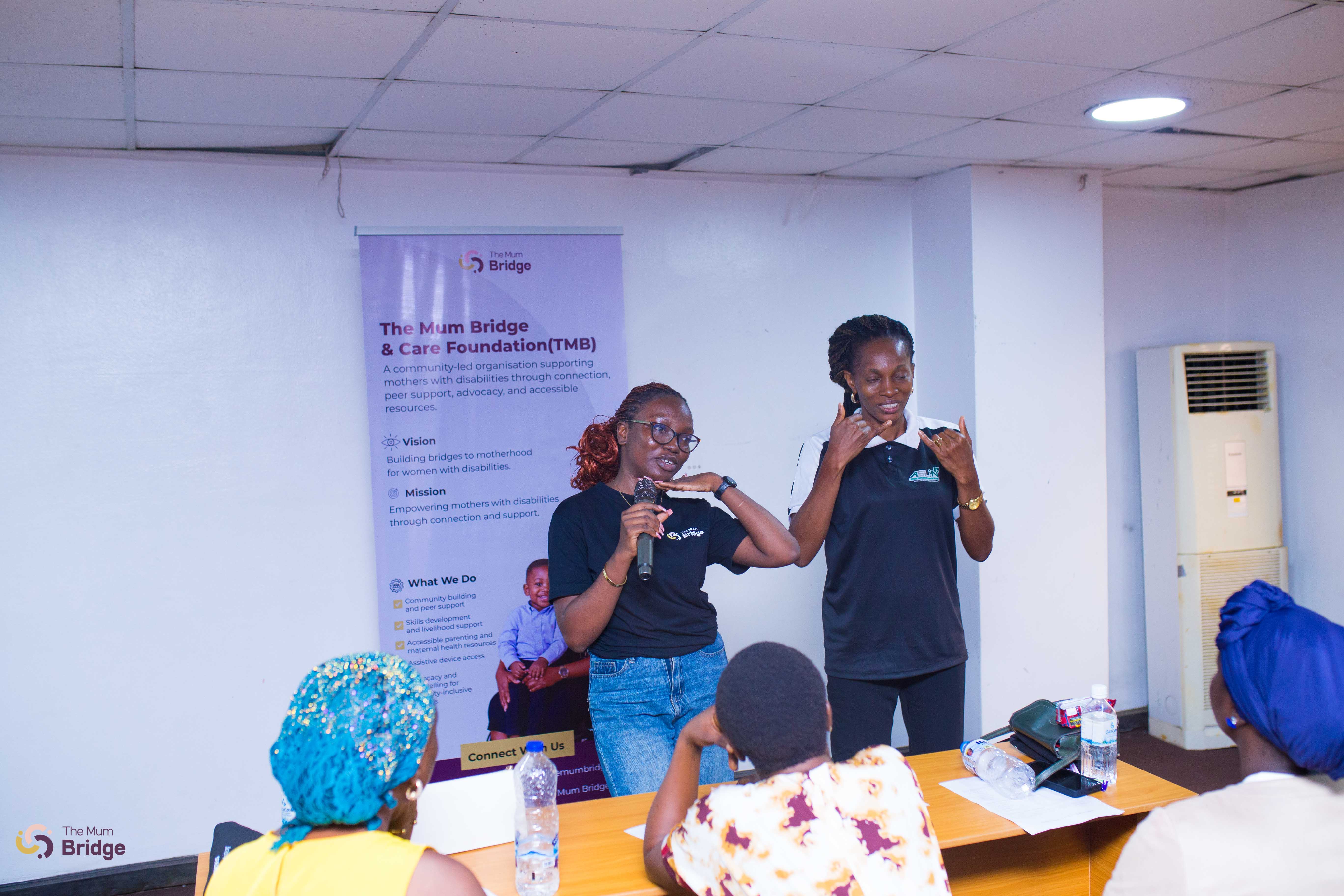 A Mum Bridge team member addresses the community with a sign language interpreter beside her, ensuring the session is accessible for deaf participants