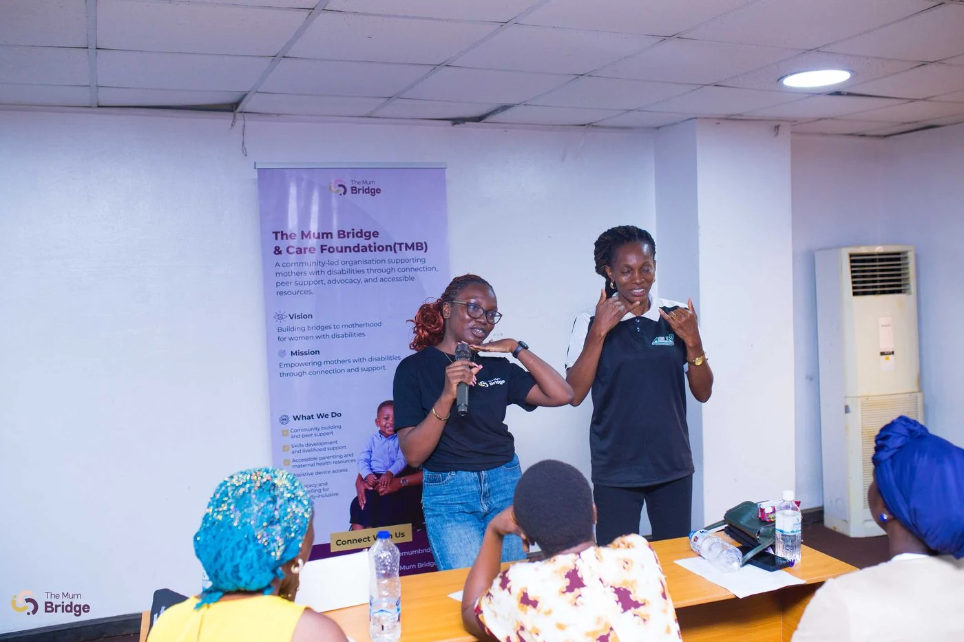 A Mum Bridge team member addresses the community with a sign language interpreter beside her, ensuring the session is accessible for deaf participants