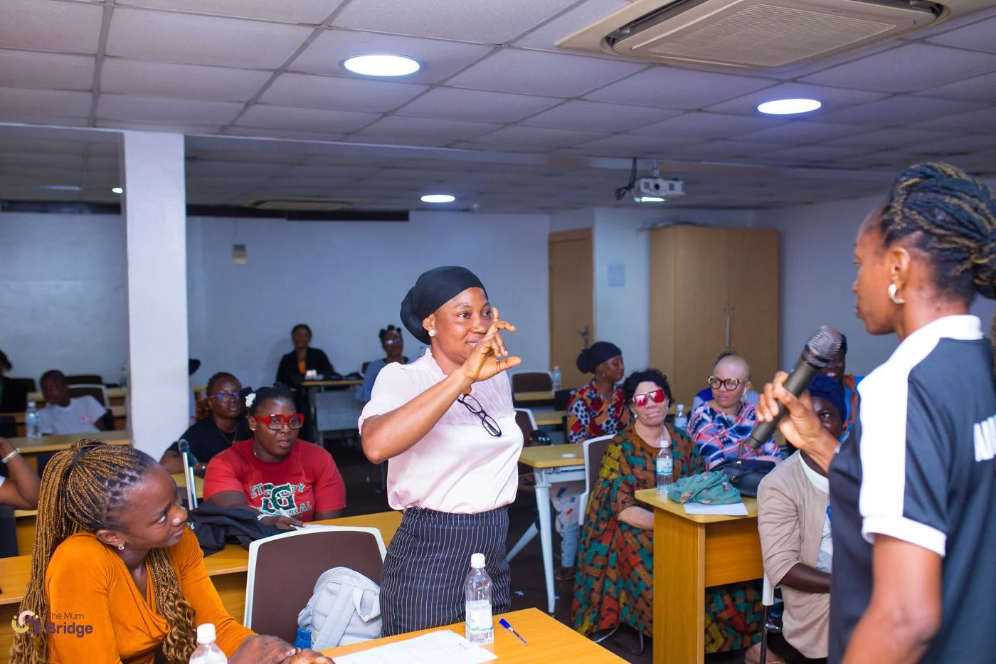 A community member stands to share her experience during an interactive Mum Bridge session, with the audience listening