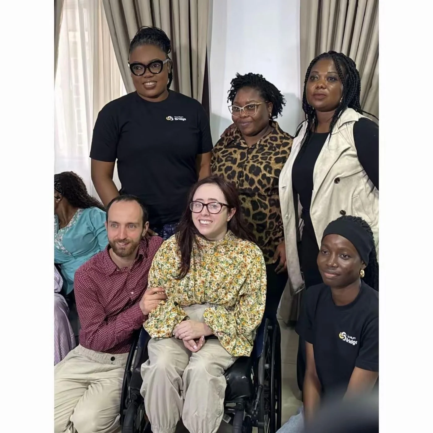 Mum Bridge team members in branded shirts standing behind visiting advocate Niamh Ni Hoireabhaird and another wheelchair user seated in front